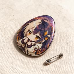 Egg-shaped raised foil glitter holographic tinplate badge photographed at a 45-degree angle showing its contoured shape and foil shine, with a butterfly pin clasp beside it